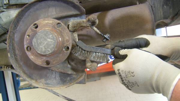 Eine Drahtbürste hilft, den Rost zu entfernen. Reinigung des Bremssattelhalters